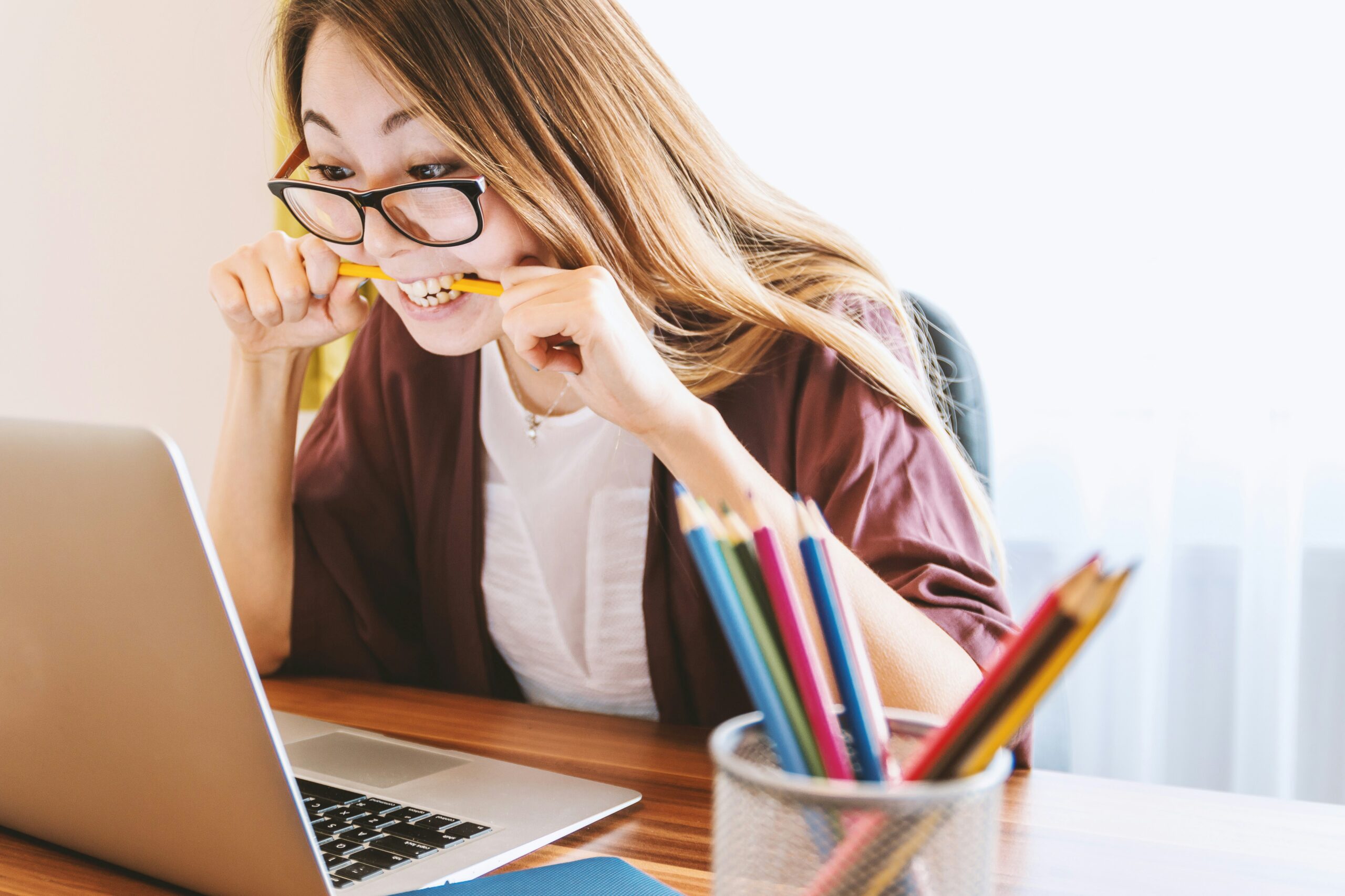 woman biting pencil while sitting on chair in front of computer during daytime